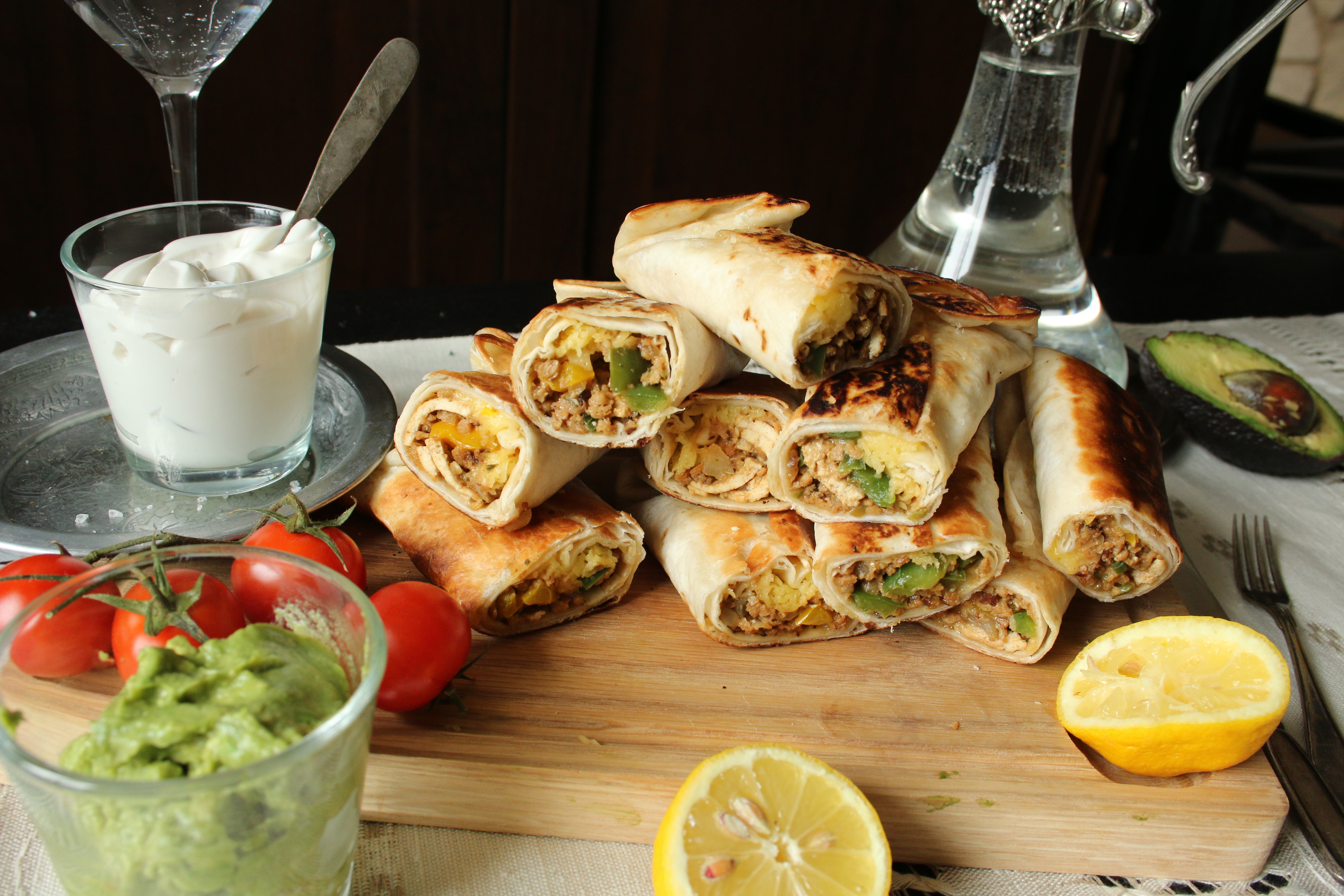 Chimichangas Chimichangas i en hög på en skärbräda, bredvid står en skål med vegansk créme fraiche och en skål med guacamole