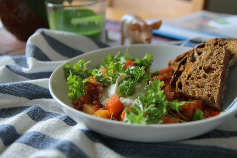 Mustig linsgulasch med kall dippsås och persilja Linsgulasch med persilja i en vit skål står på ett bord med rutig duk