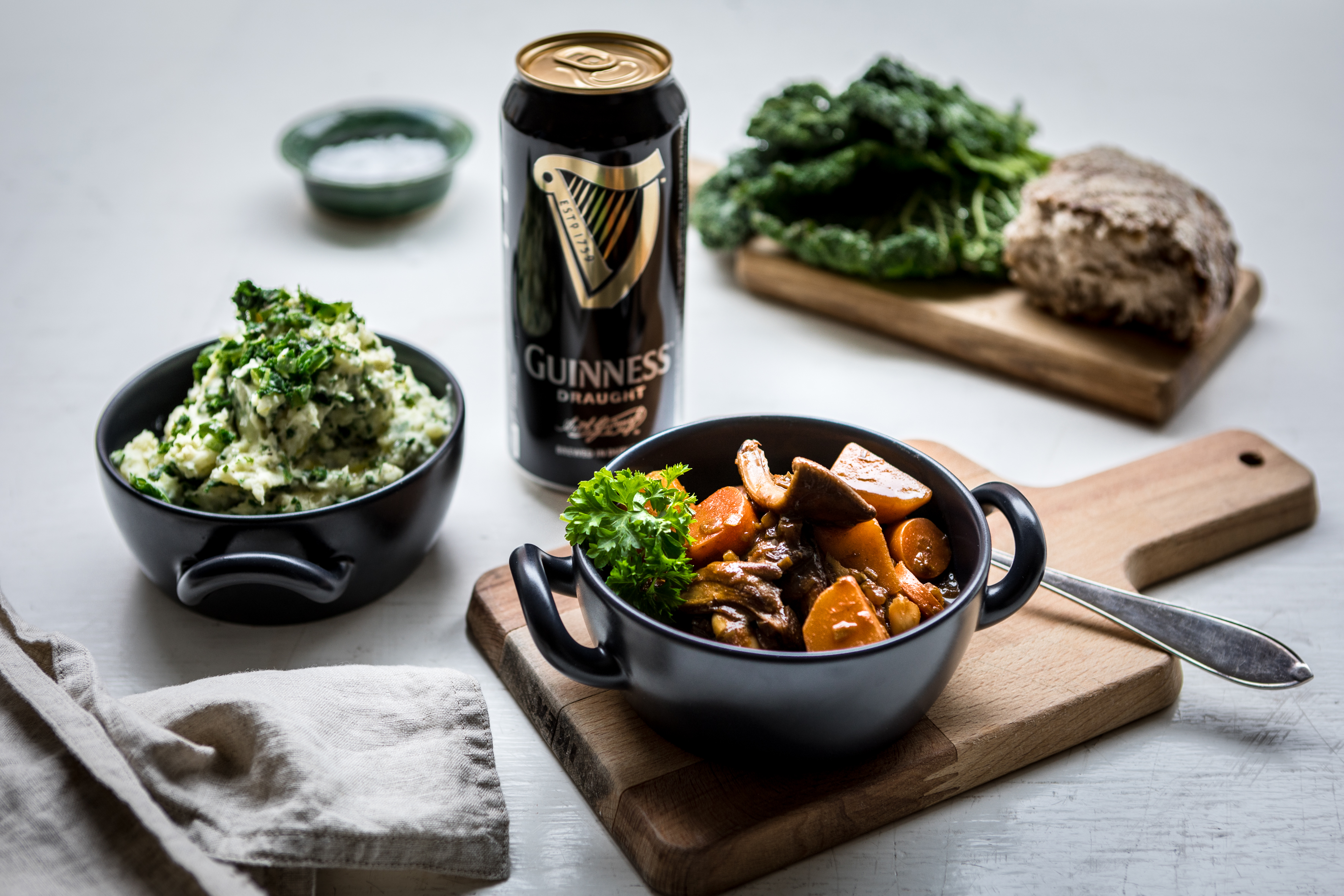 Irish stew En skål med Irish stew står på en skärbräda bredvid en skål med irländskt potatismos och en öl