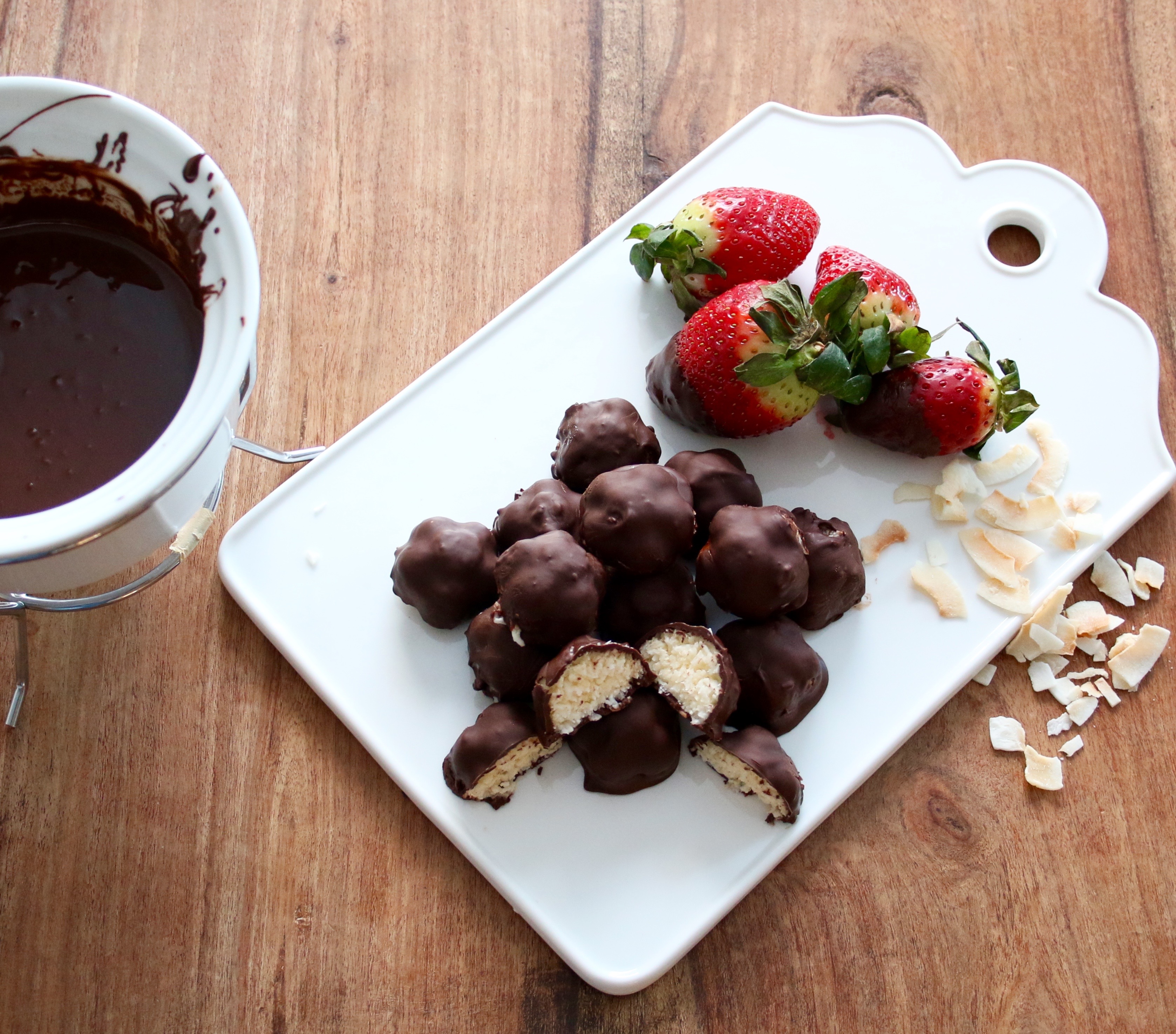 Smarriga chokladbitar med kokos Chokladbitar med kokosfyllning på en vit skärbräda, bredvid ligger några jordgubbar och kokosbitar