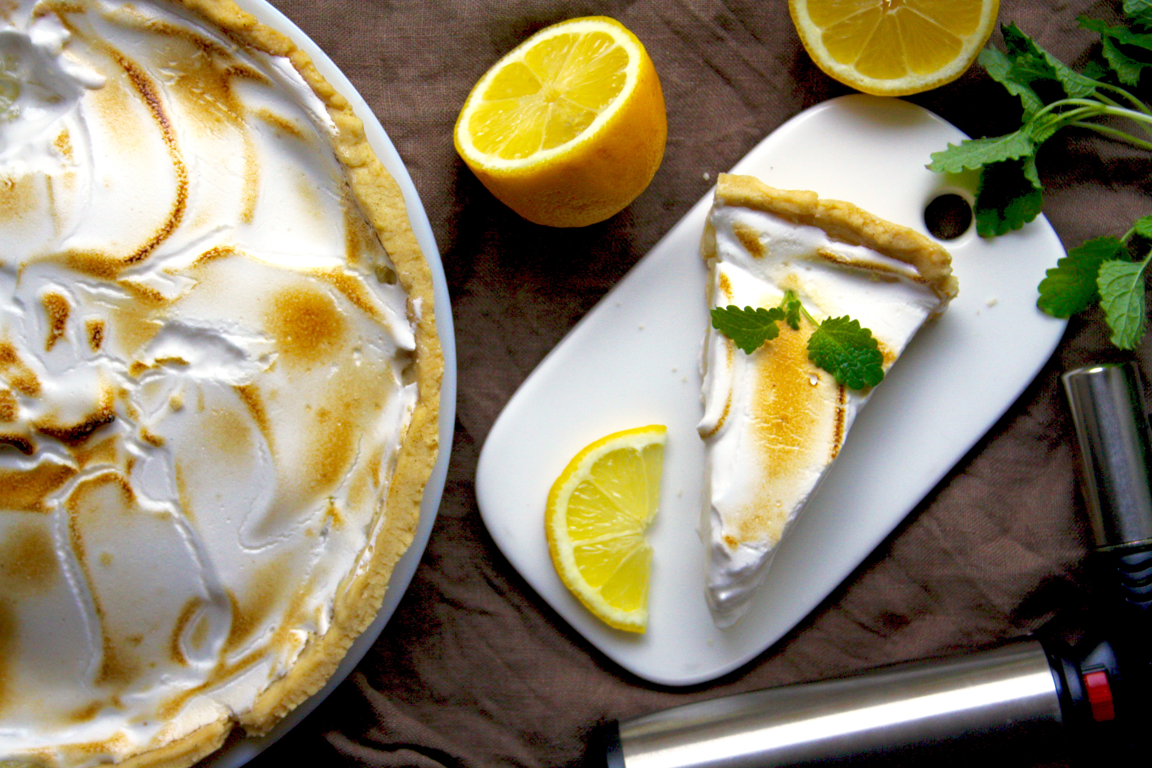 Syrlig citronpaj med vegansk maräng En citronpaj med marängtäcke, bredvid pajen ligger några delade citroner