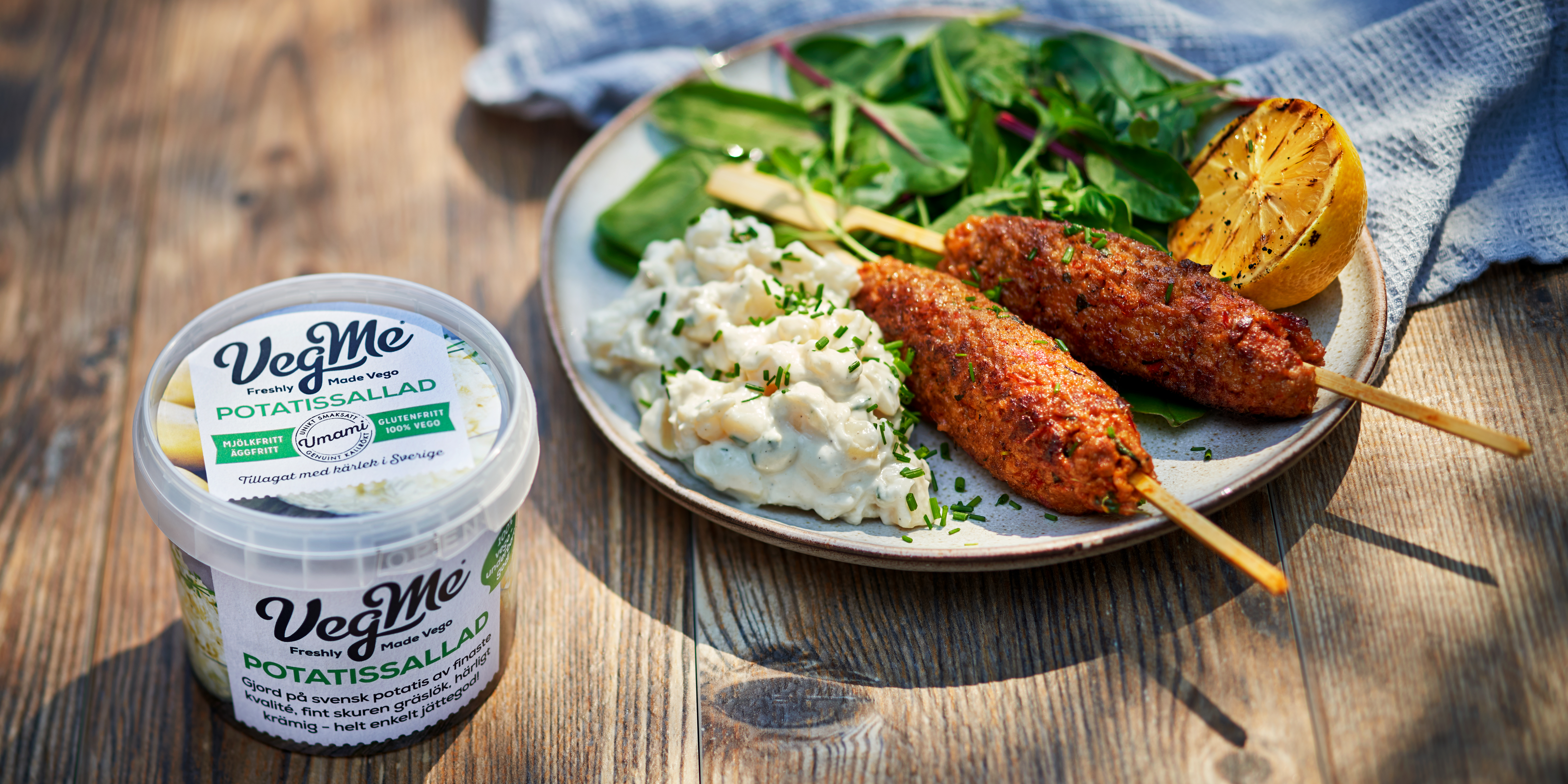 Förpackning av potatissallad intill en tallrik med potatissallad med vegansk spett