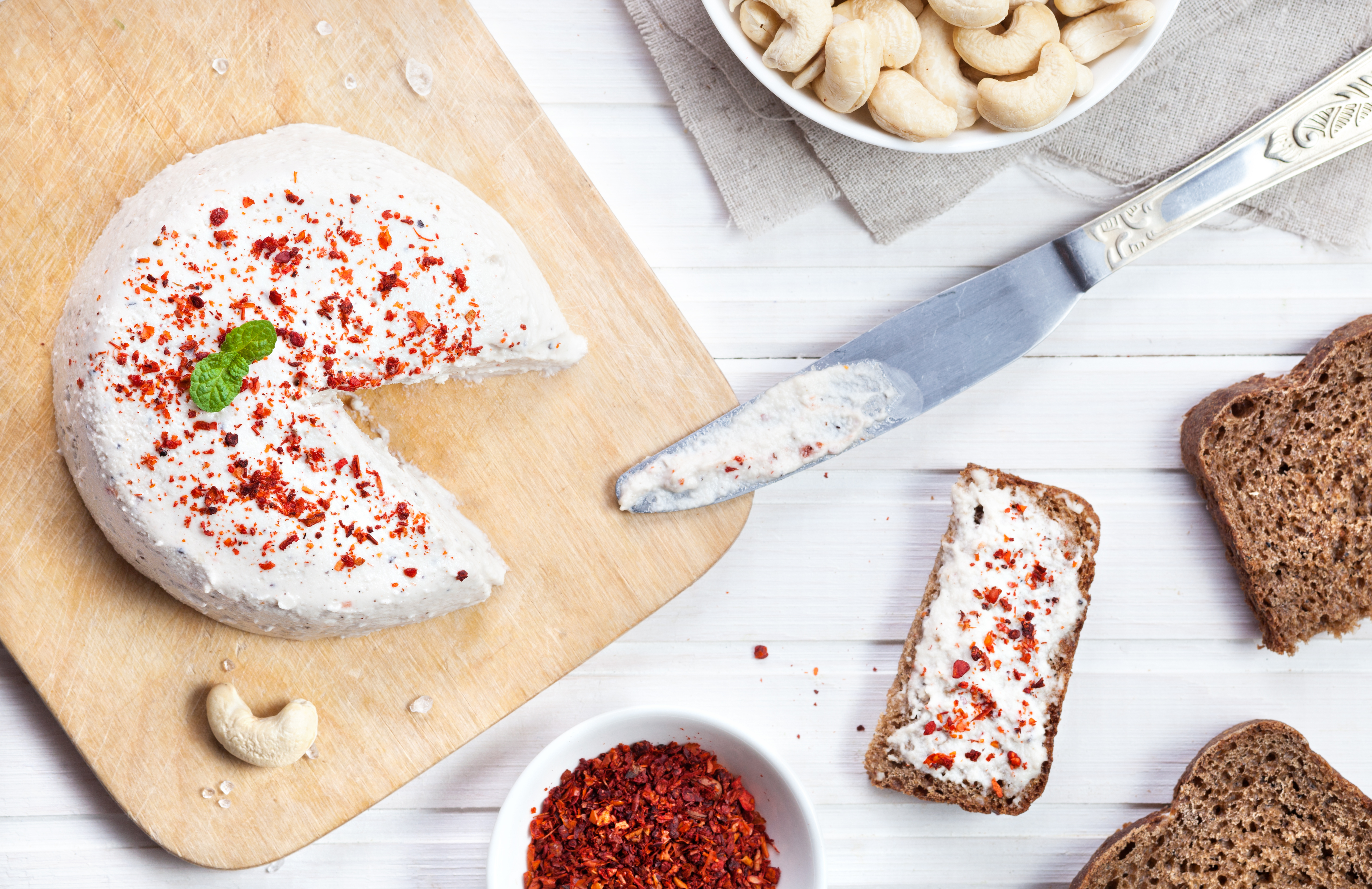 Egengjord cashewost Vegansk cashewost toppad med chiliflingor på en skärbräda.