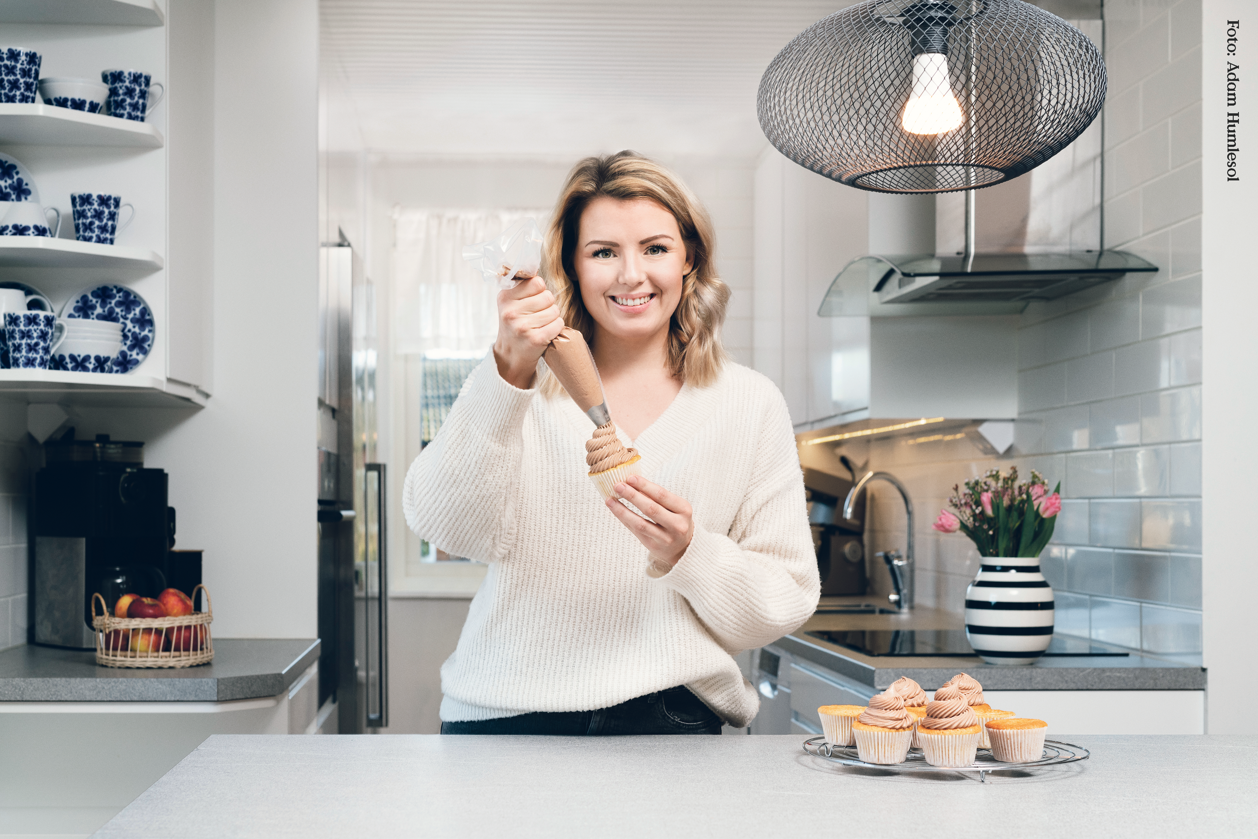 Frida Svanberg står i sitt kök och spritsar muffins