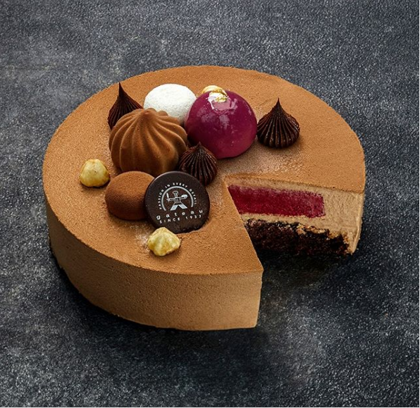 Foto: Gateau En brun rund tårta där en bit har tagits så att innehållet med svartvinbär och mousse syns. Toppat med dekorationer från Gateau