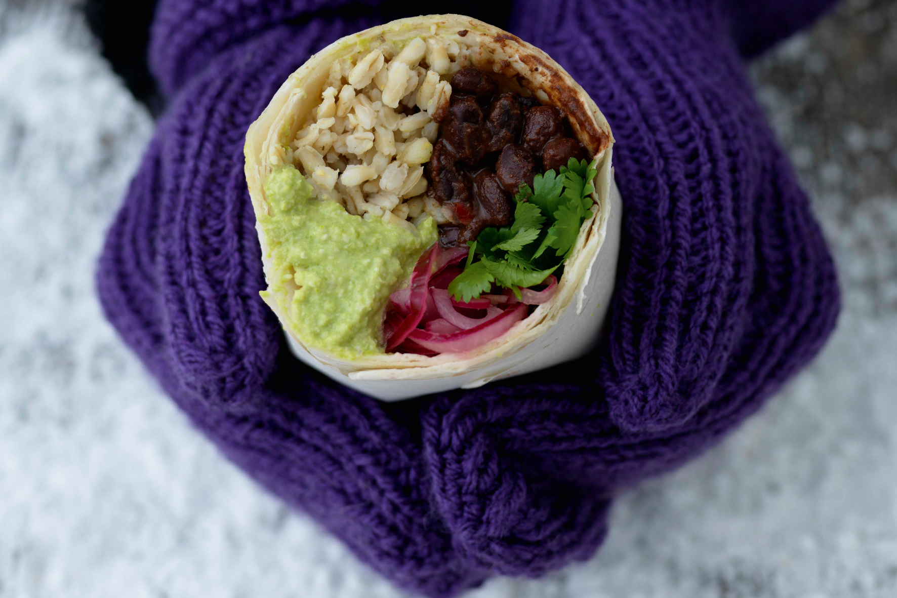 Foto: Ulrika Pousette händer med lila vantar håller i en burrrito med krämiga svarta bönor, guacamole och ris