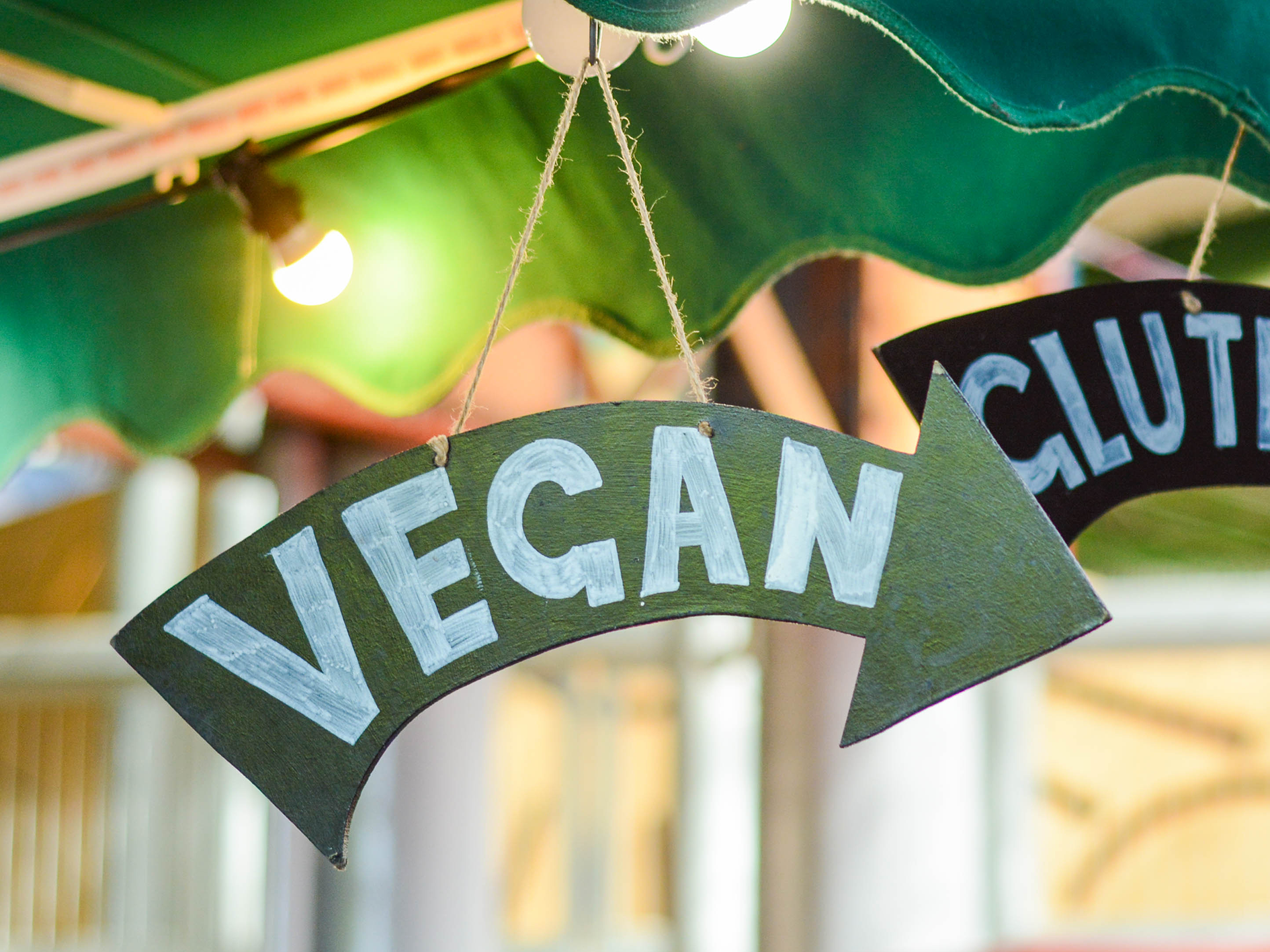 Foto: olesea vetrila / Shutterstock Pilformad skylt med texten "vegan", hängandes från ett parasol i dovt upplyst miljö.