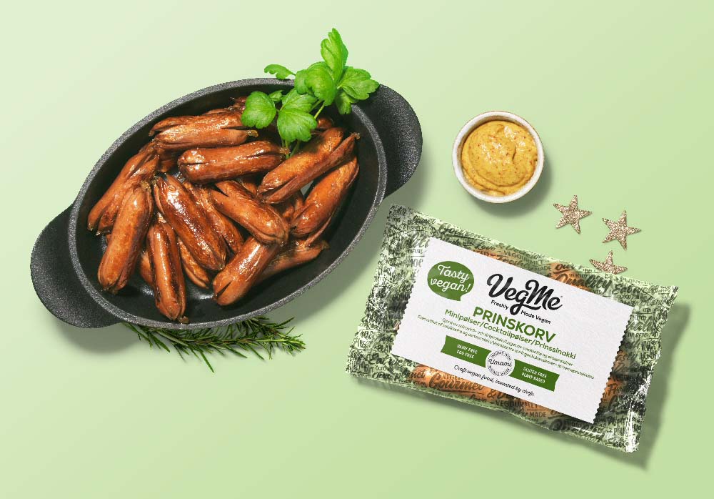 Foto: VegMe Prinskorv från VegMe i gjutjärnsgryta mot grönbakgrund, med förpackning och en liten skål senap bredvid.