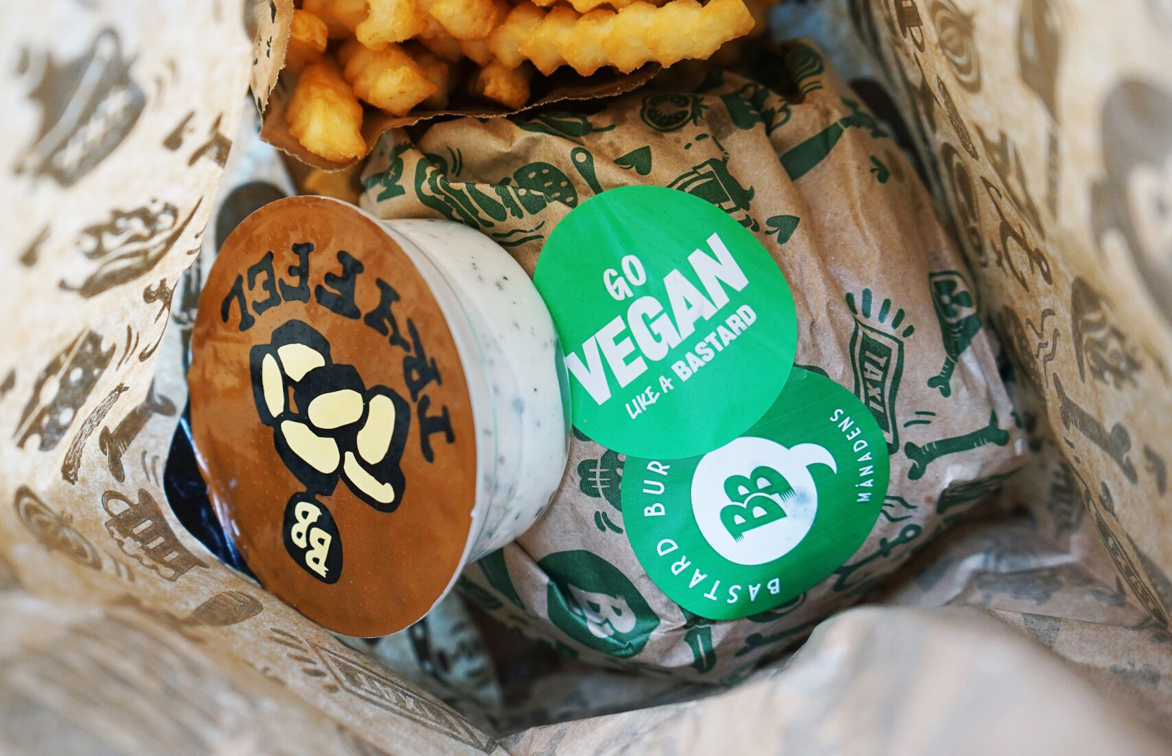 Foto: Bastard Burgers Burgare, pommes och sås från Bastard Burgers i papperspåse. På burgaren finns ett klistermärke med texten "Go vegan like a bastard".