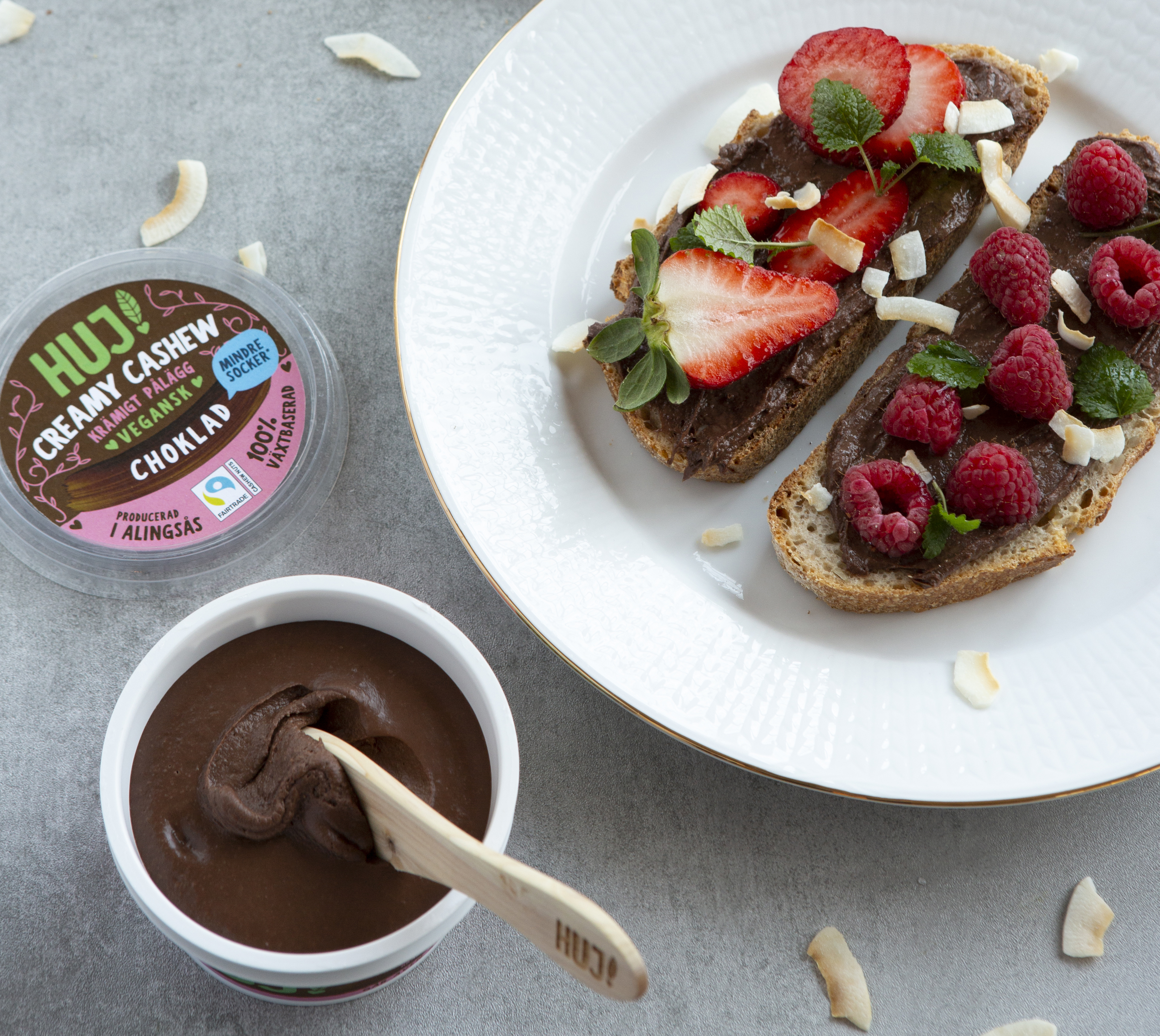 Foto: Huj HUJ Creamy Cashew Choklad i öppnad förpackning till vänster. Till höger på macka med bär och kokos.