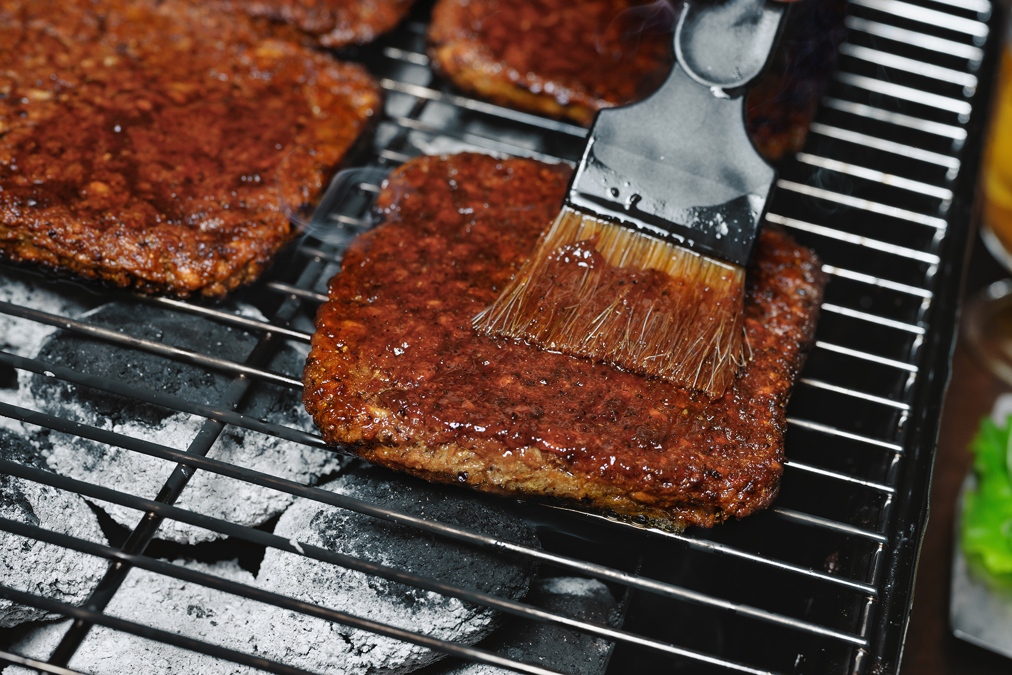 Produktfoto: Stackys Fyrkantiga veganska burgare på en grill som blir penslad med grillolja.