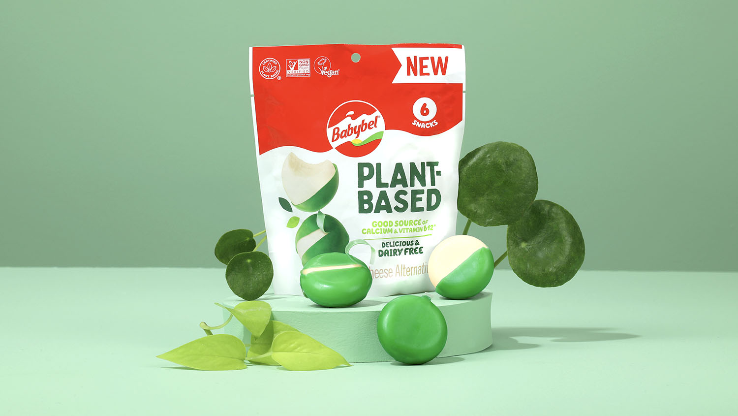 Produktfoto: Bel Group Växtbaserade Babybel-ostar i grönt vax framför produktpåsen mot en grön bakgrund.