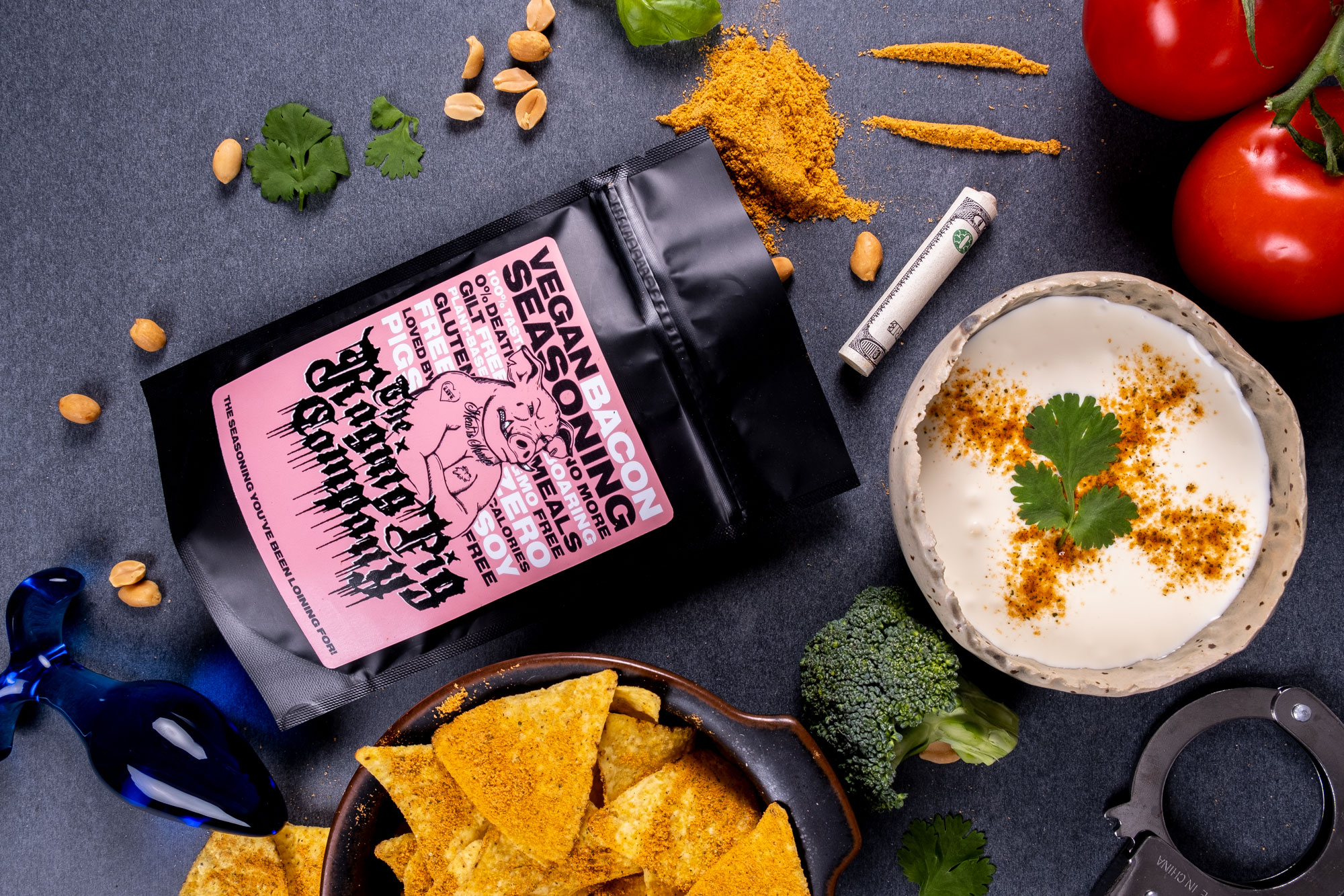 Produktfoto: The Raging Pig Company Kryddpåse, dip och nachos utplacerade på ett svart bord.