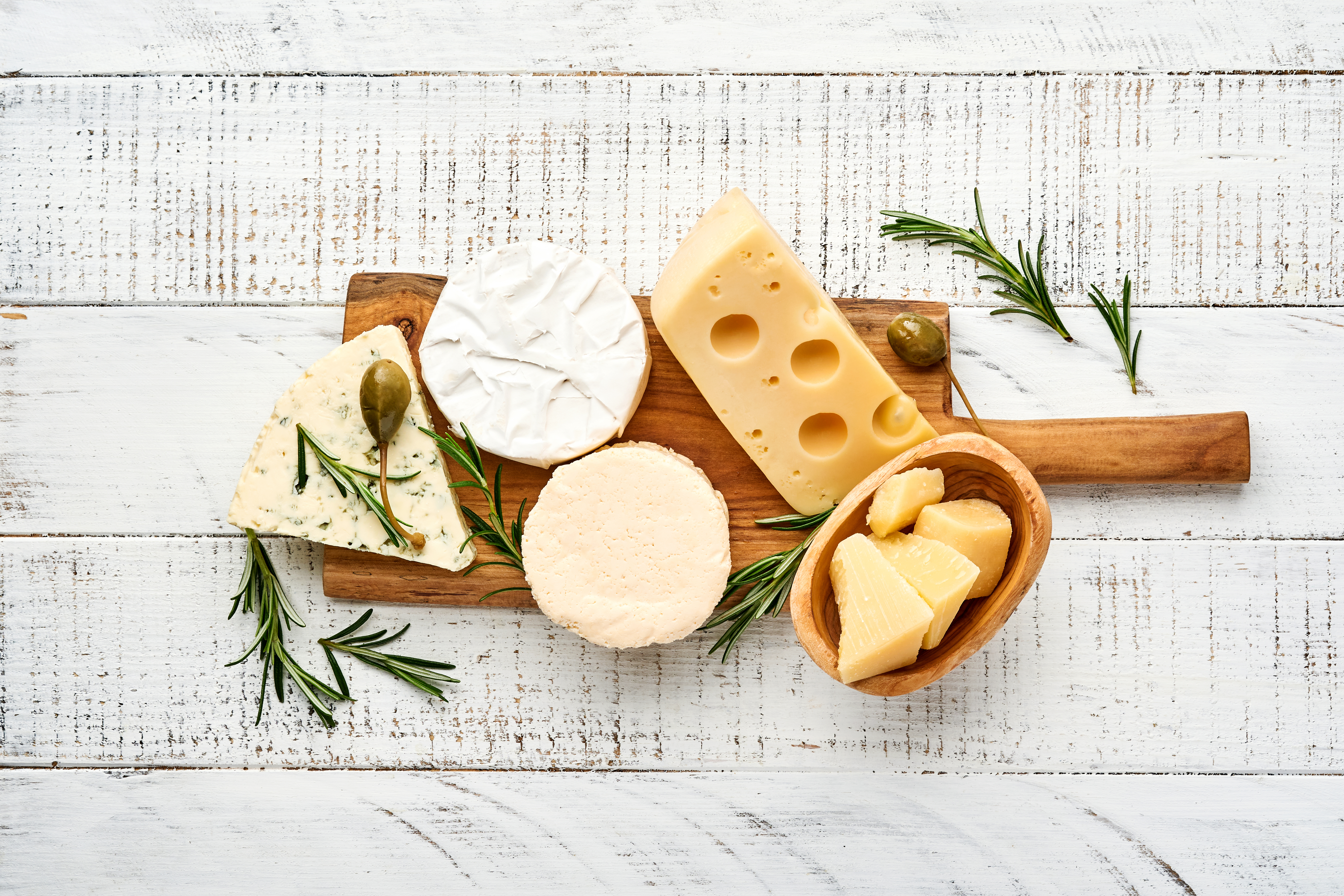 Foto: Katarzyna Hurova / Shutterstock Flera olika mejeriostar på en träbricka på ett vitt bord.