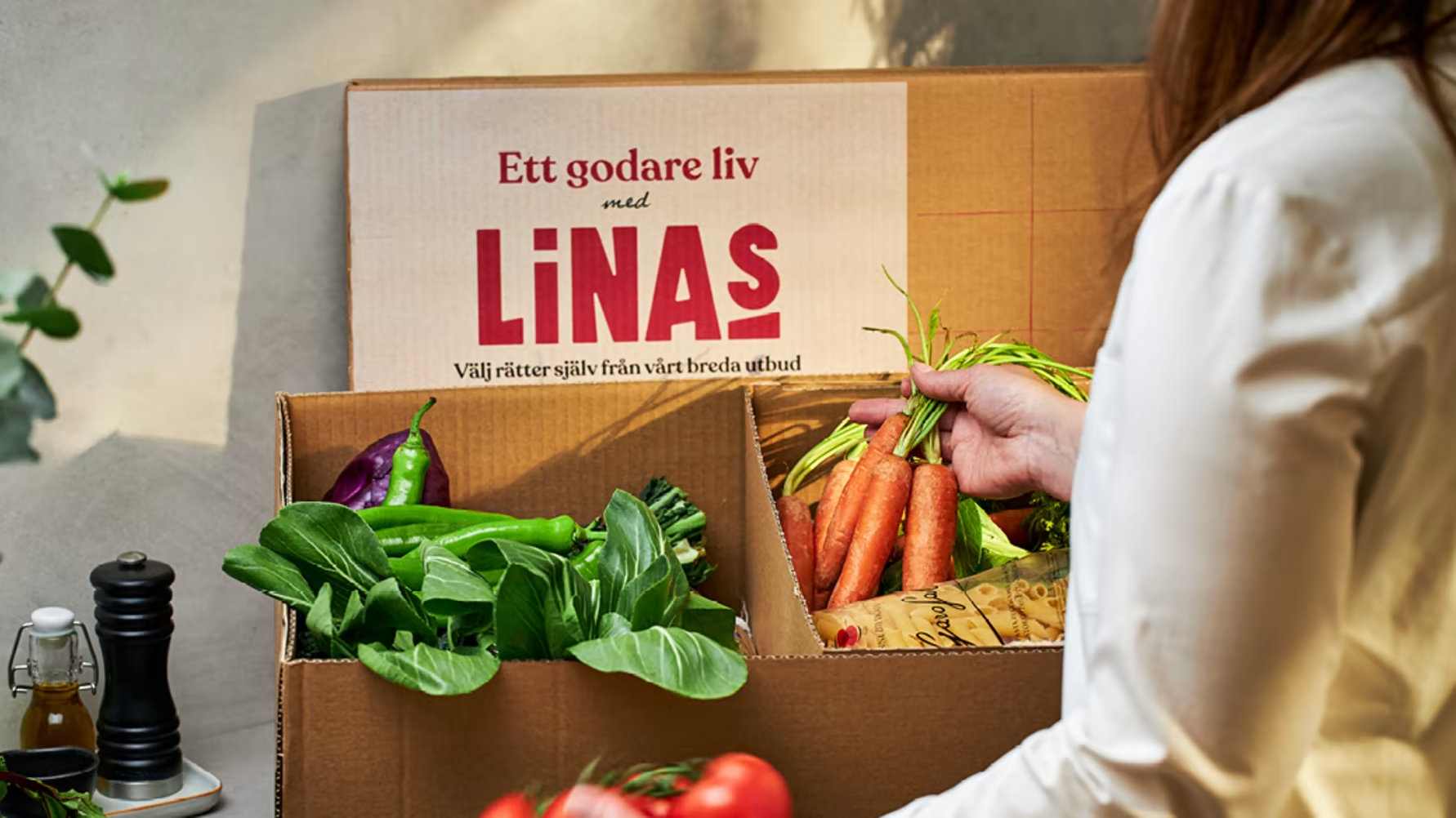 Produktfoto: Linas Matkasse En kartong från Linas Matkasse med olika grönsaker och råvaror i.