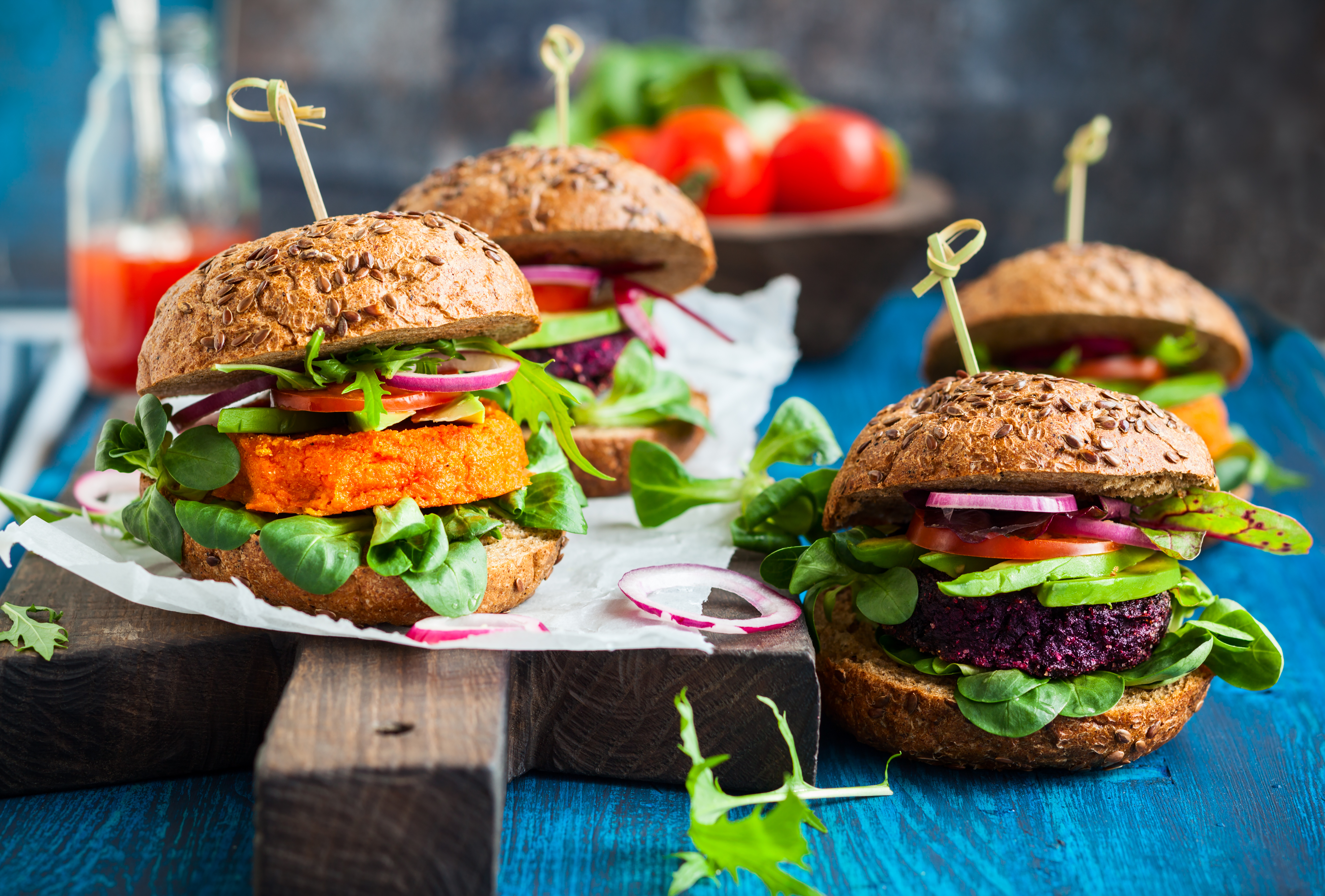 Foto: Kolpakova Svetlana/Shutterstock Fyra växtbaserade burgare med mycket grönt på ett blått bord.