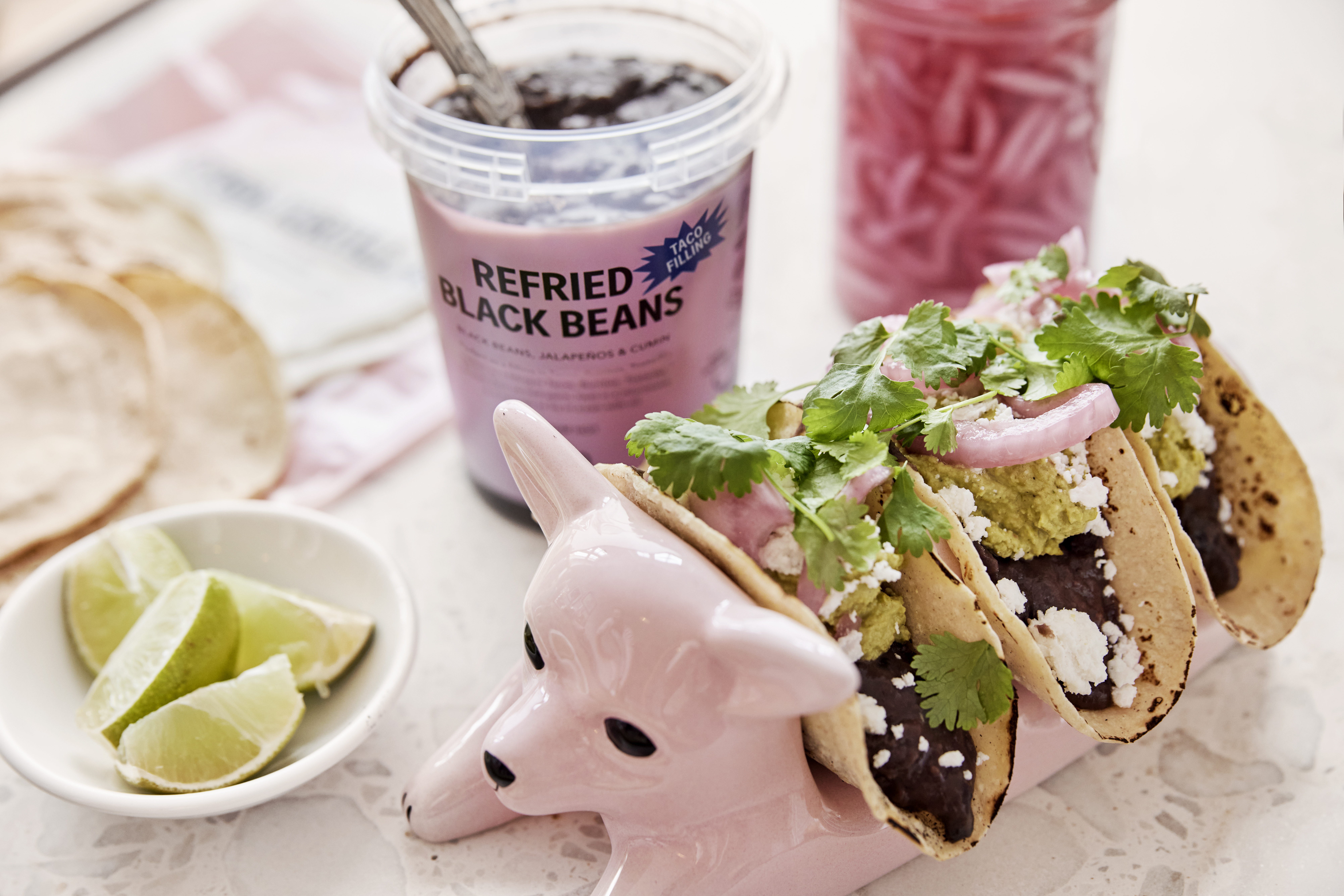 Produktfoto: El Taco Truck Mjuka fyllda veganska tacos uppställda i en keramikhund med läsk, lime och picklad rödlök på sidan om.