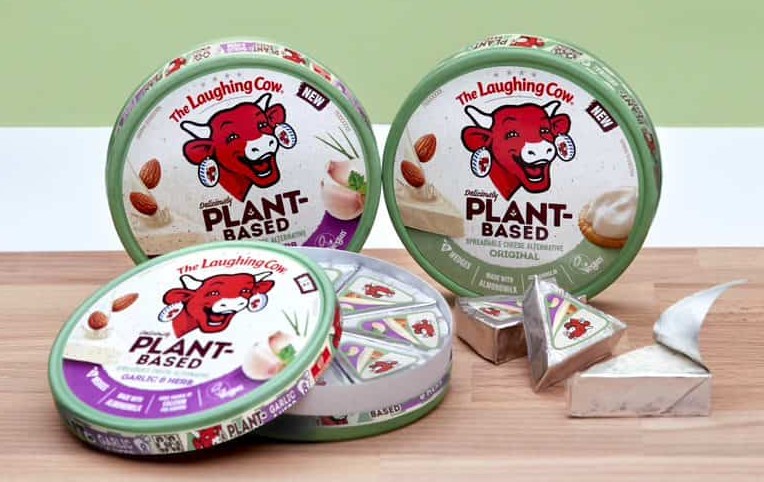 Produktfoto: Bel Group USA Tre hjul med vegansk mjukost i uppställda på ett träbord mot en ljusgrön vägg