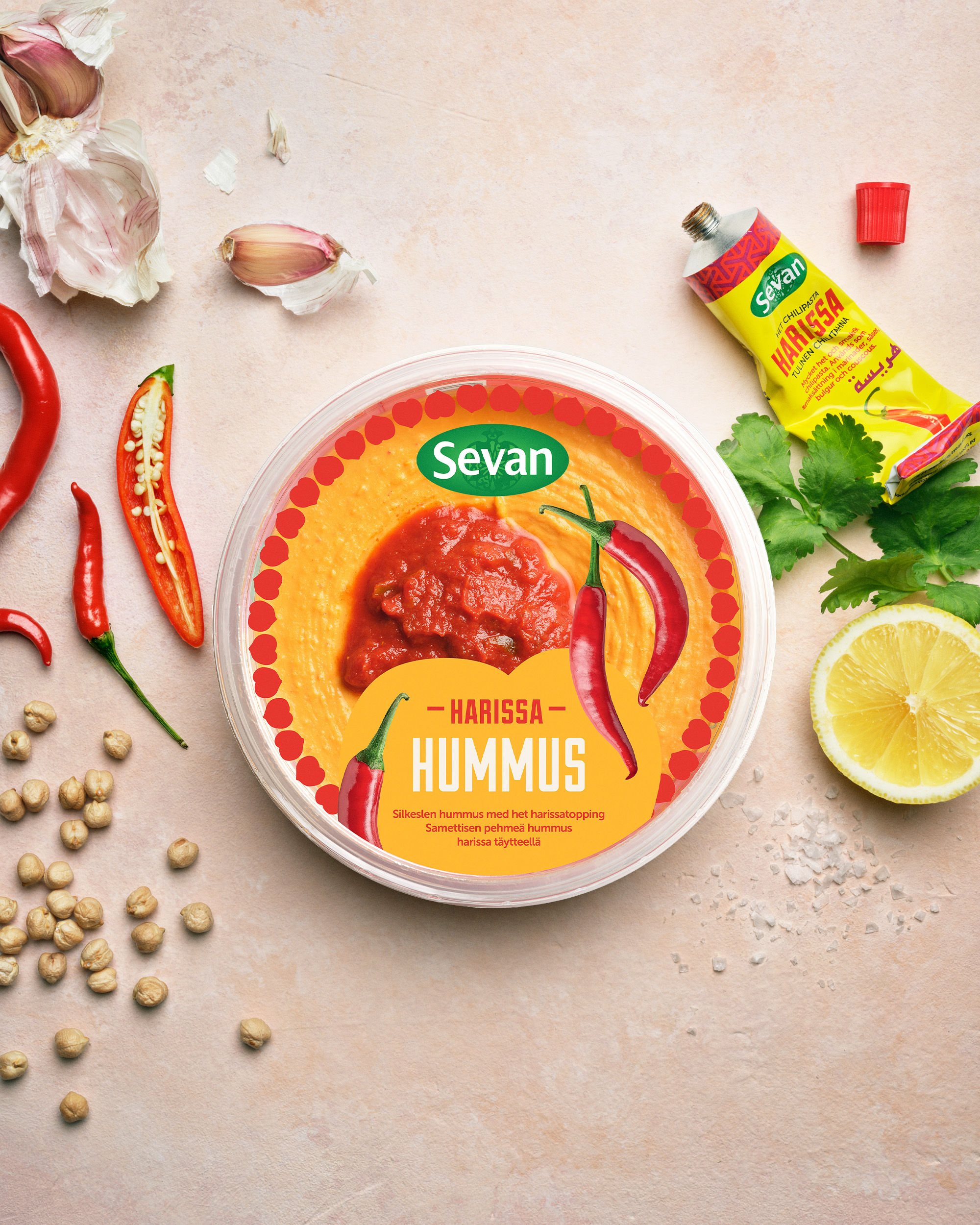 Produktfoto: Sevan En burk med hummus på ett bort med citron, mynta, vitlök och kikärtor runt