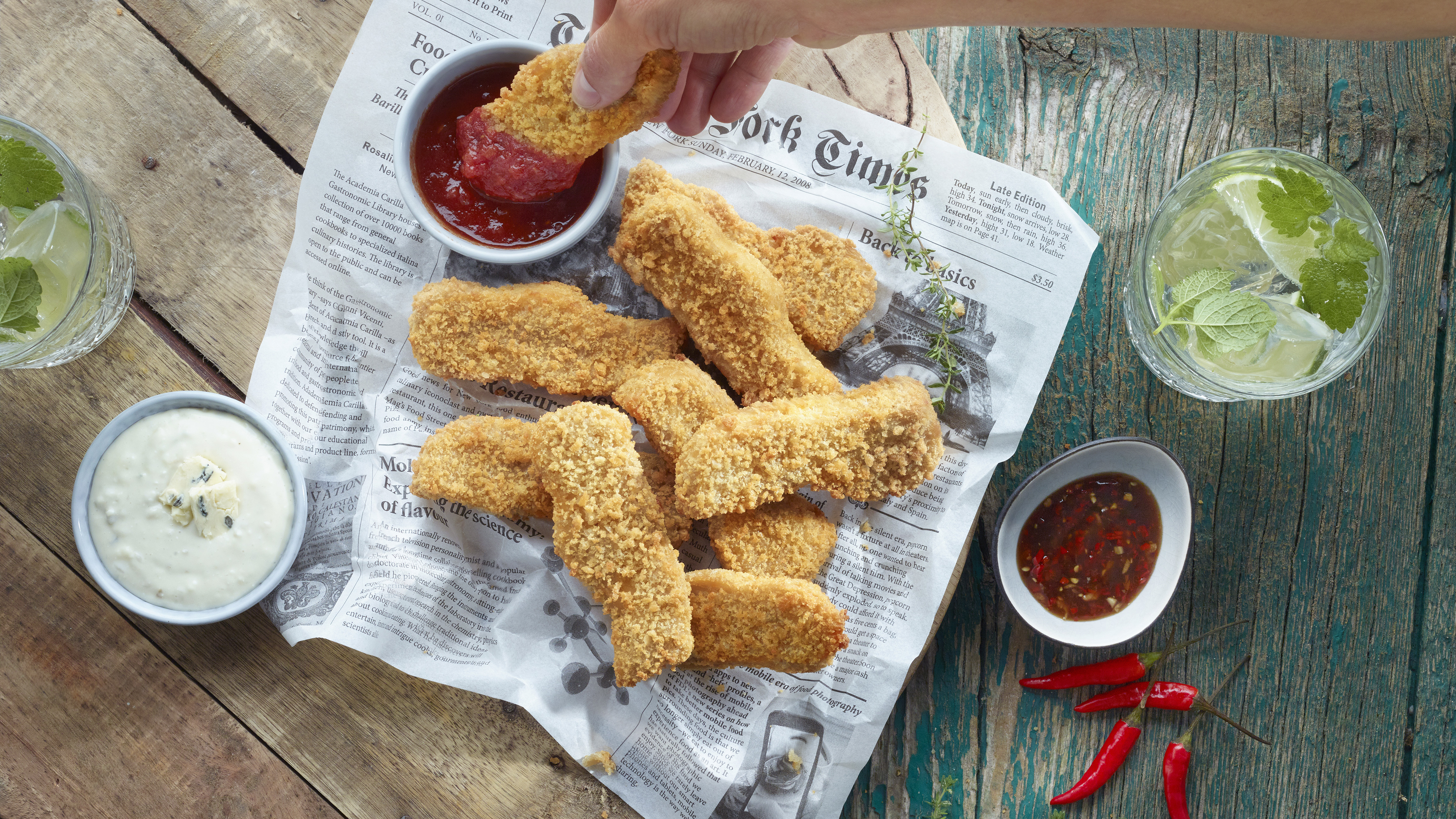 Produktfoto: Hälsans Kök Veganska chicken fingers på ett tidningspapper med massa dippar runt om.
