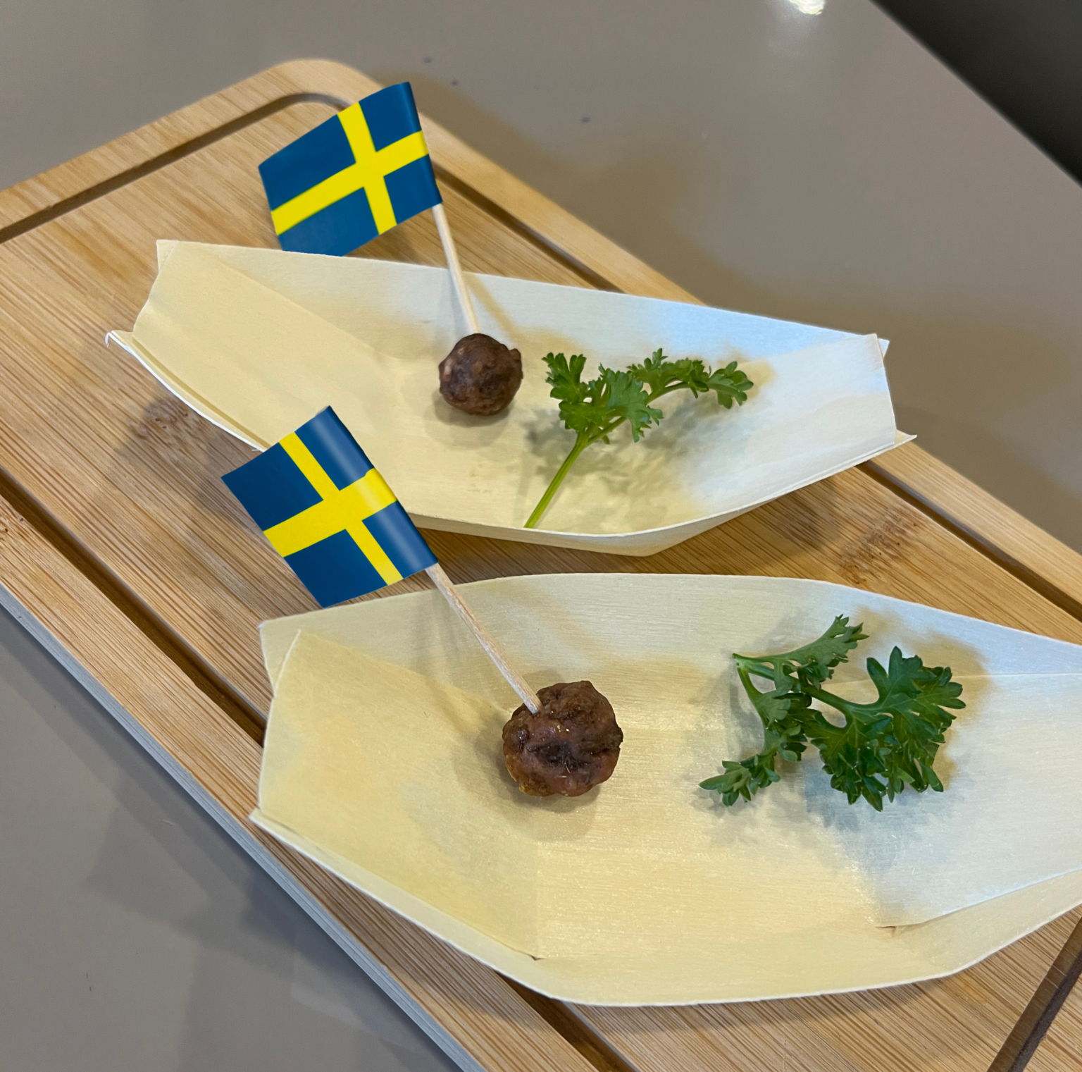 Produktfoto: Re:meat Två odlade köttbullar på vita fat med små svenska flaggor i och kvistar med persilja på sidan om