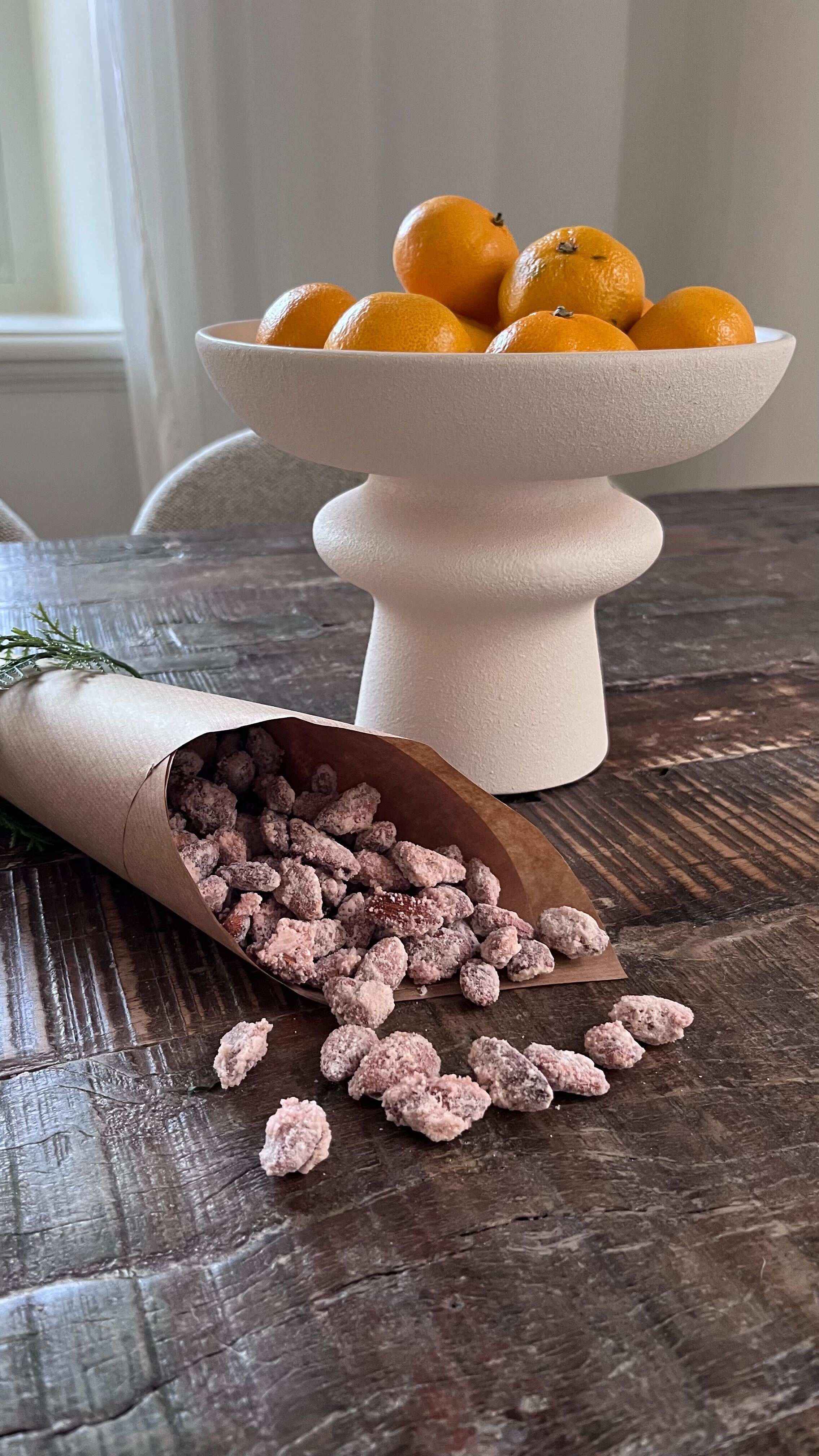 Foto: Rebecca Johansson en pappstrut med brända mandlar som ligger på ett träbord. En vit keramikskål med satsumas i bakgrunden.