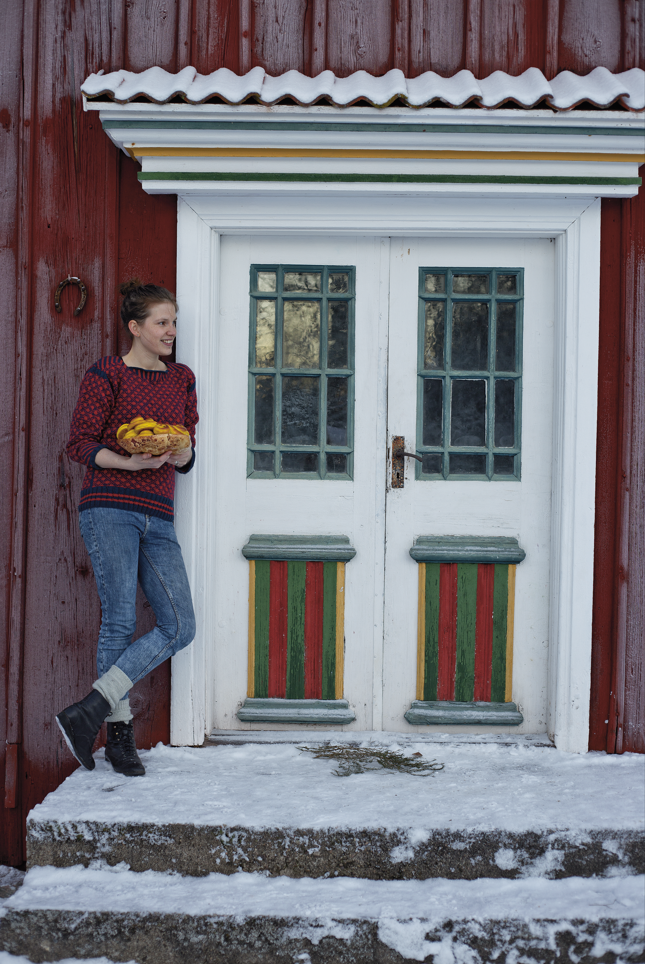 Foto på Karolina Tegelaar Kvinna som står lutan mot en röd vägg på ett hus