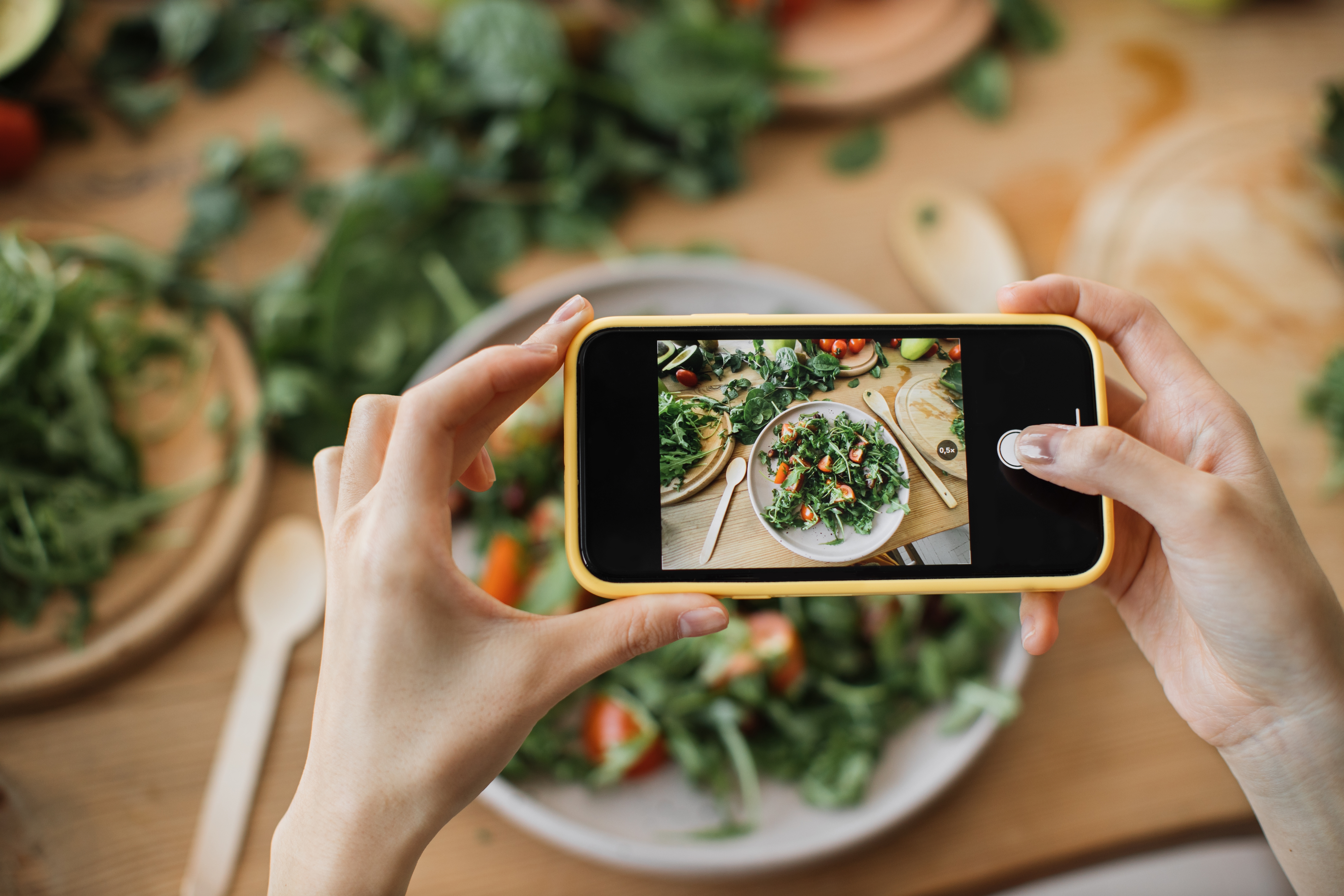 Foto: SofikoS/Shutterstock Kvinnahänder tar telefonfoto av matlunch eller middag. Grönsakssallad, avokado, ruccolatomater. Smartphonefotografering för sociala nätverk. Vegetarisk hälsosam mat.