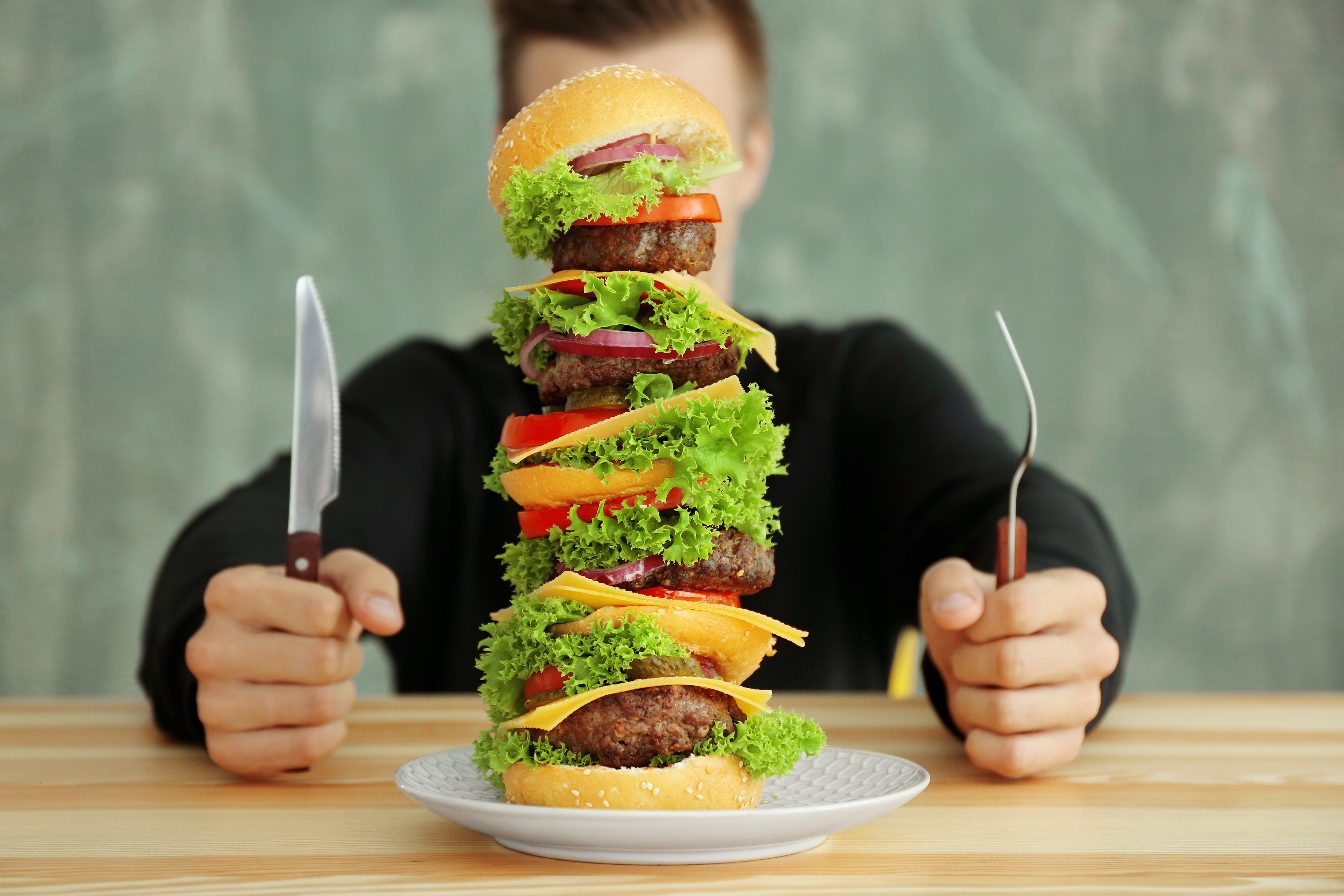 Foto: Africa Studio/Shutterstock Man äter en stor hamburgare vid ett bord