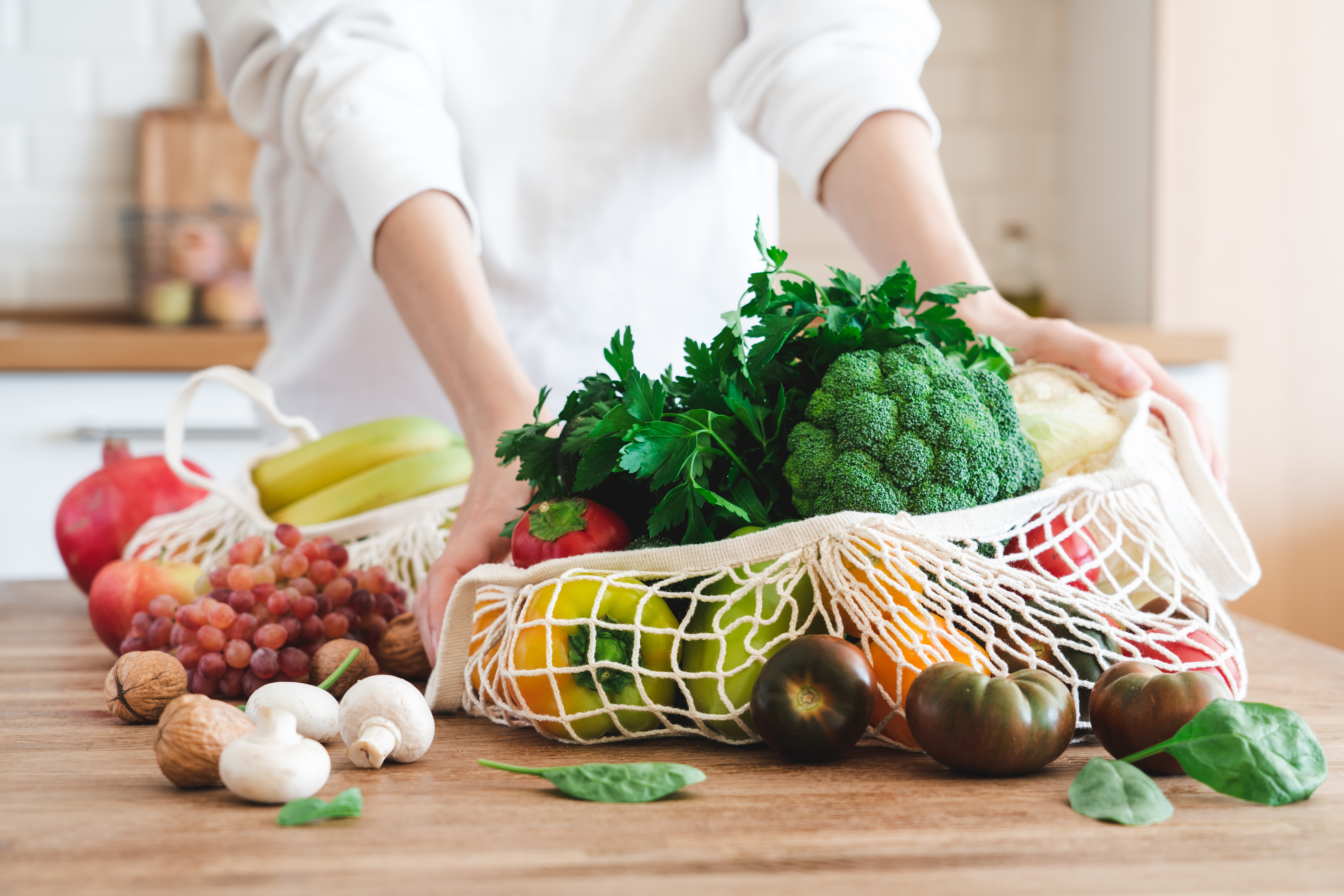 Foto: Anna Puzatykh/Shutterstock Fruits and vegetables in cotton reusable net mesh bag on wooden table in modern bright kitchen. Organic vegan food set. Sustainable lifestyle concept