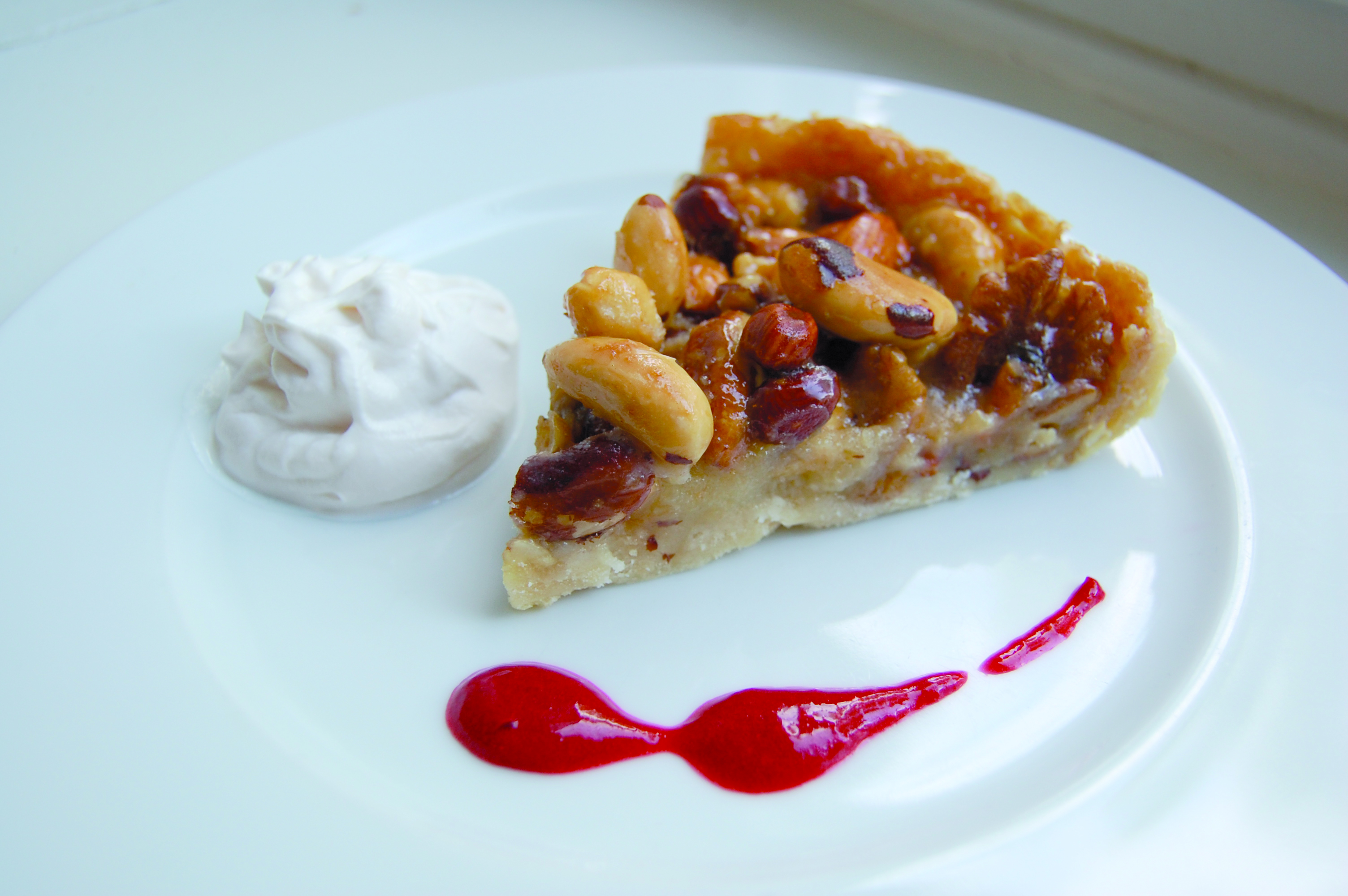 Vegansk nötpaj med vaniljgrädde och hallonsås Vegansk nötpaj med vaniljgrädde och hallonsås på en vit tallrik