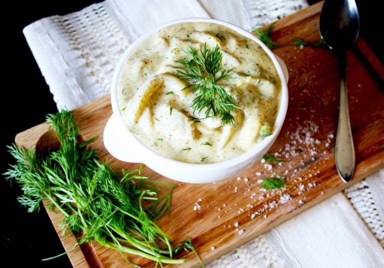 Auberginesill i senapssås i en skål på en skärbräda, garnerad med dill. 