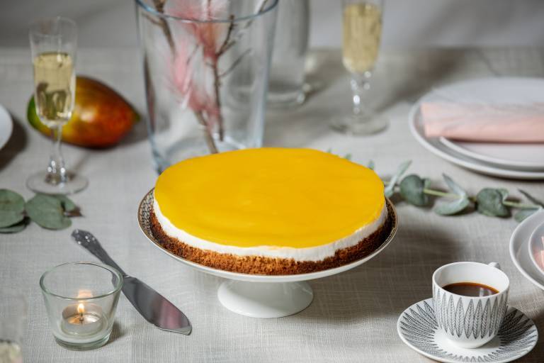 Vegansk cheesecake med mangoglasyr på ett tårtfat.