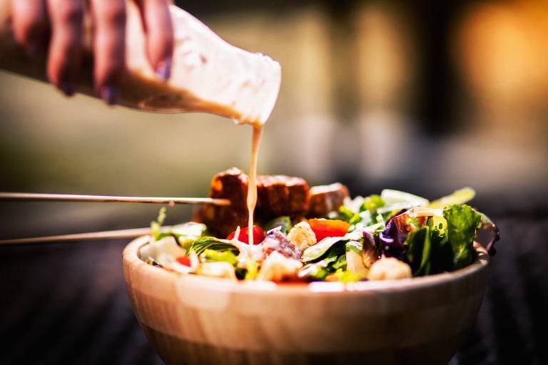 Vegansk caesarsallad med tempeh och en hand som häller på dressing 