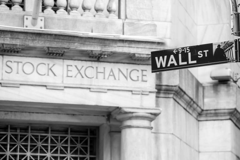 Bild på vägskylt med texten "wall st" framför en mur med texten "Stock exchange"