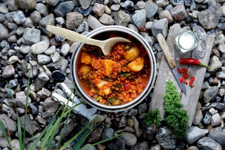 Potatis one pot i en gryta på småstenar med en träbräda med en kniv, röd chili och flingsalt bredvid