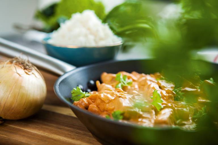 Vegansk korvstroganoff i stekpanna. I förgrunden färska örter och i bakgrunden en skål ris.