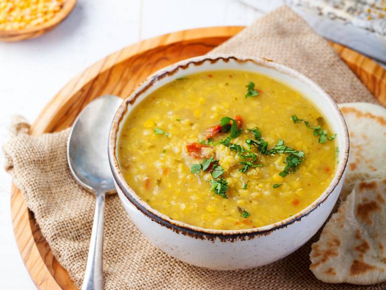 Daal i djup skål på ett bord, med naanbröd bredvid.