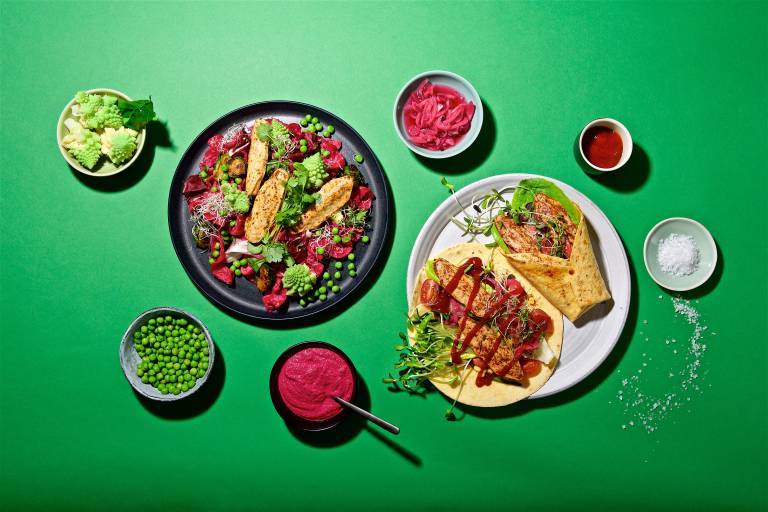 veganska filléer i en sallad på en tallrik och en i wrap på en annan tallrik uppdukat på ett grönt bord med tillbehör. 