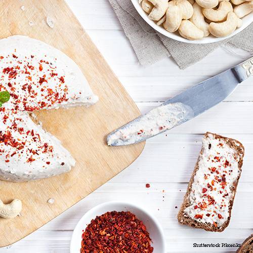 Rund cashewost med paparikakrydda på en skräbräda där en triangel har skurits ut. 