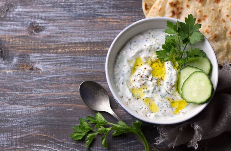 Vegansk tzatziki i en skål till höger i bild mot ett mörkt träbord