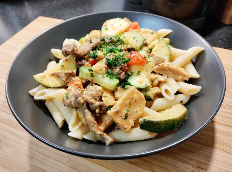 Vegansk kyckling- och kantarellpasta i en mörkgrå djuptallrik på ett bord av ljust trä. 
