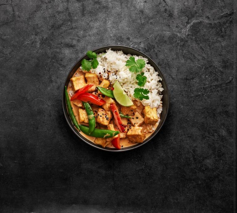 röd currygryta med ris i en djuptallrik vinkel uppifrån mot en granitgrå bakgrund