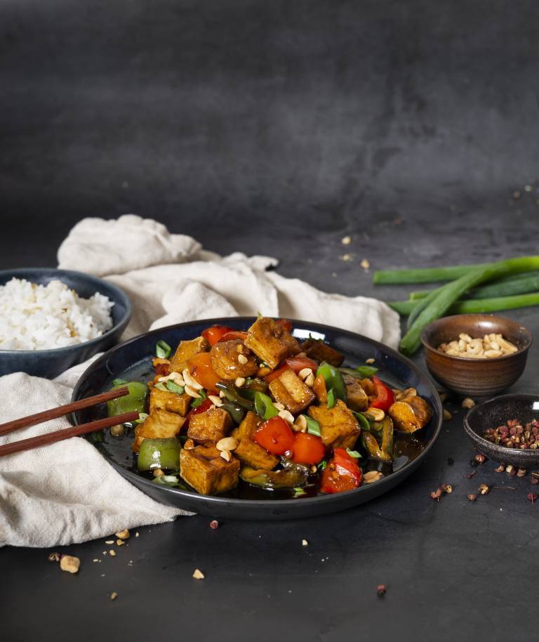 Kung Pao rätt i djuptallrik på en kökshandduk mot en mörkgrå bakgrund