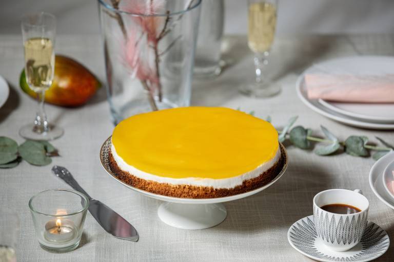 mangocheesecake på ett tårtfat mitt på ett bort med linneduk