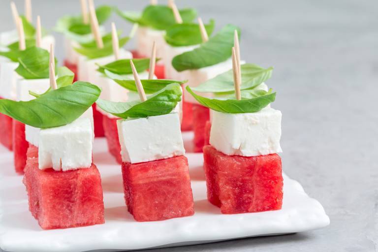 Snittar med melon, vegansk fetaost och basilika på ett vitt fat. 