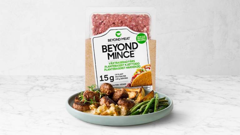 Ett paket växtbaserad färs bakom en tallrik mat på ett marmorbord. 