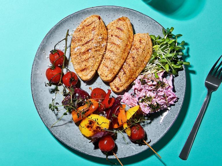 tre vegofiléer med grönsaksspett och coleslaw på en tallrik, på ett turkost bord