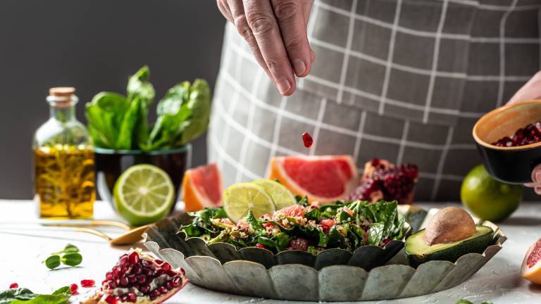 En växtbaserad sallad på ett fat och en hand som slänger i granatäppelkärnor