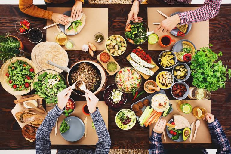 Bild på matbord taget ovanifrån där flera händer plockar vegansk mat 